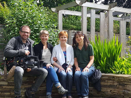 Image of Sophia and Julie and the film crew for 'Love Your Garden' sat on the curved stone seat
